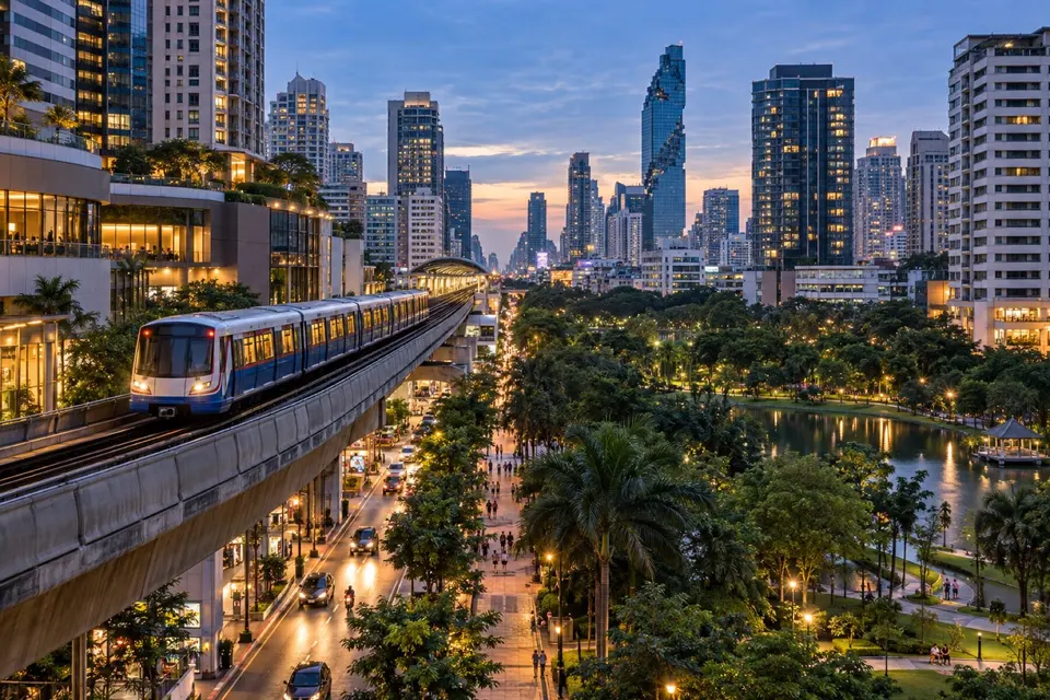 BTS Skytrain passing central Bangkok buildings and a green city park at blue hour