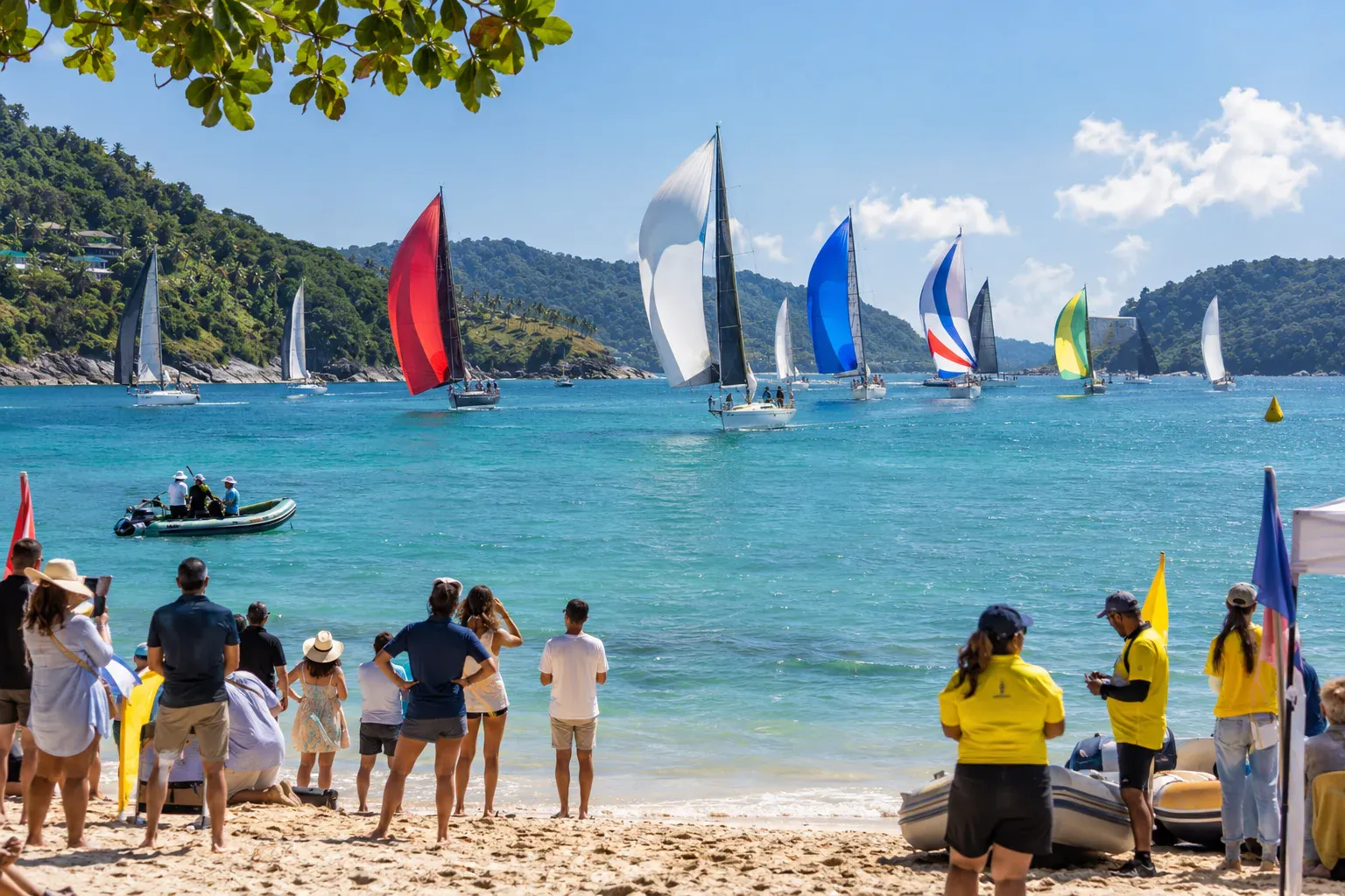 Sailboats racing across a Phuket bay while spectators watch from the beach